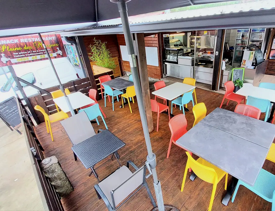 La terrasse couverte du snack, tables et chaises colorées face au comptoir